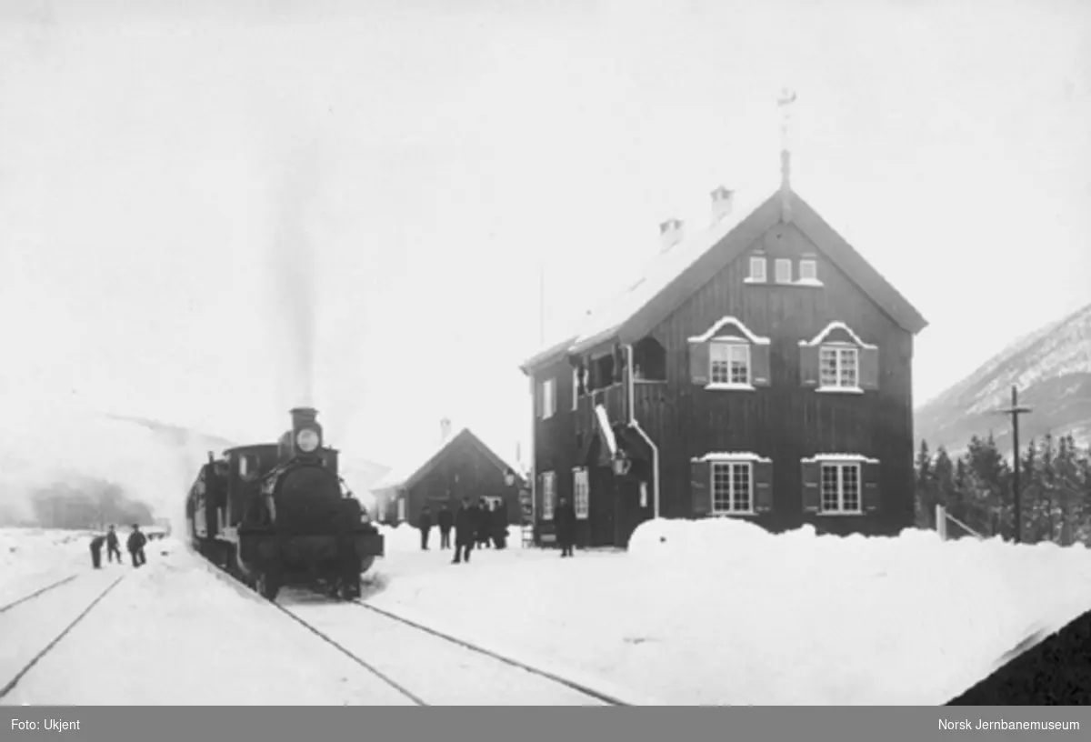 Vinterbilde fra Brennhaug stasjon med stasjonspersonalet på plattformen og et damplokomotiv av type 11 med persontog i spor 1