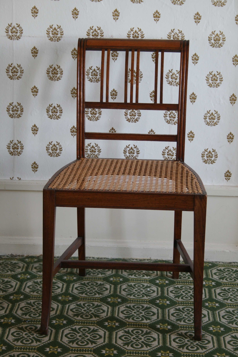 Spinkel stol i mahogni, med rottingsete, smale spiler i ryggen. 5 stoler og 1 kanapé