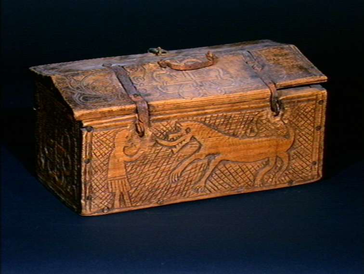 Skrin med flate sider of lett takformet lokk. Hengslet i bakkant og låsmekanisme i forkant. Håndtak midt på lokket. Hele utsidenhar skurd dekor med ranker, dyr og mennesker.