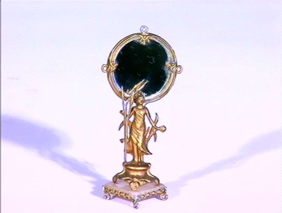 Dukkehus inventar, speil i tinn forgylt med marmorplate. Sokkel på speilen er kvatratisk og speilen holdes av en kvinnefigur.