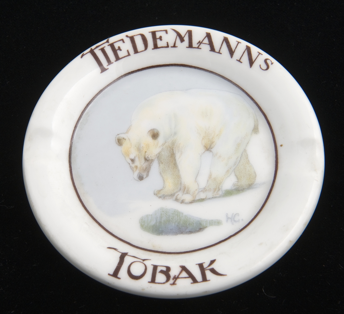 Lite, rundt askebeger i porselen med to fordypninger i randen. Påtrykket motiv av en isbjørn etter original av Halfdan Gran.