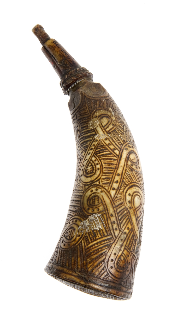 Krutthorn med flat bunnplate i tre med innskrift. Ornamentikk på horn i form av et bånd som går i løkker rundt hornet mot en bakgrunn av streker med hakk.