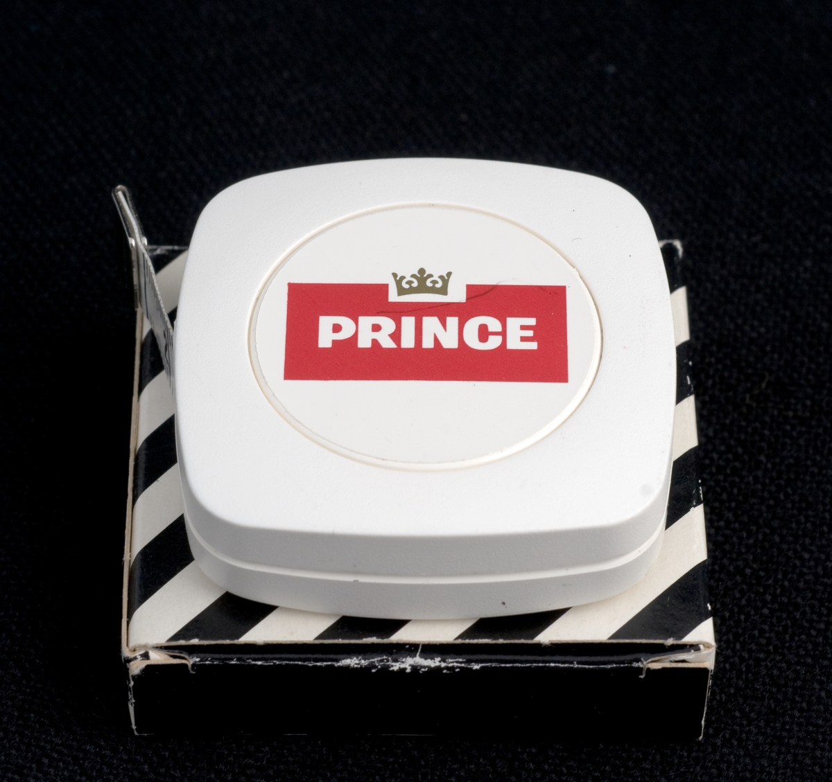 Målebånd i eske med reklame for Prince sigaretter.