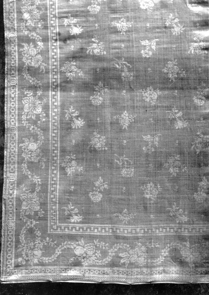 Hvit damaskserviett med småblomstret mønster, bord av guirlander og blomster. Antagelig fra Tyskland slutten av 1700-tallet.