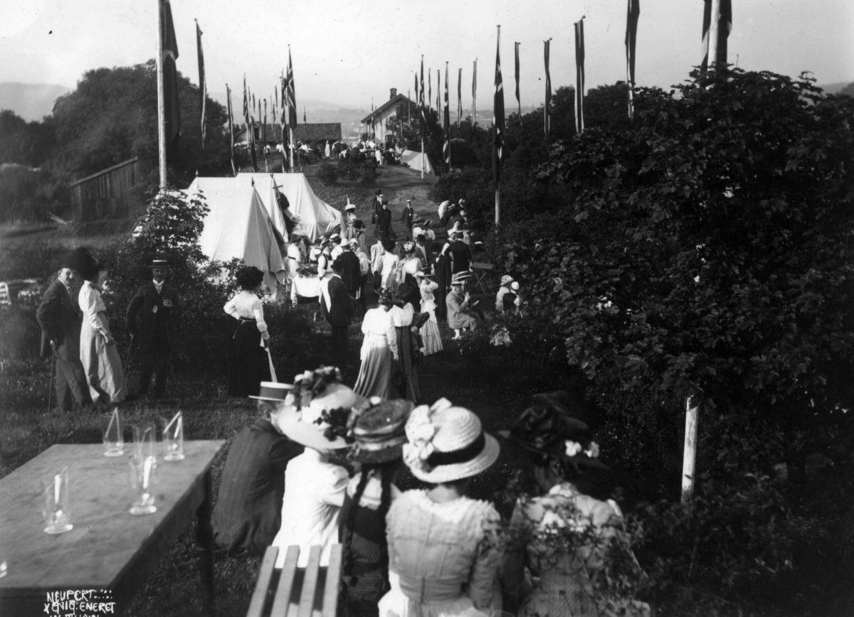 Hovedøya, Oslo. 1910. Sommermotiv. Fest. Kvinner og menn festkledd. Telt. Flagg. Bebyggelse.
