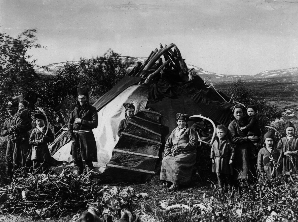 Barn og voksne samlet utenfor et telt. Middagsfjäll, Kalls Lappby før 1892. Fjell og vidde i bakgrunnen.