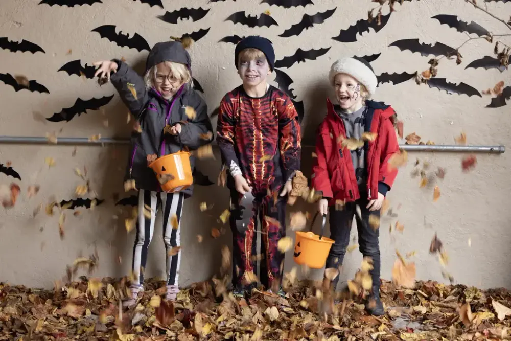 Tre barn er utkledte og leker med løv på Halloween på på Norsk Folkemuseum