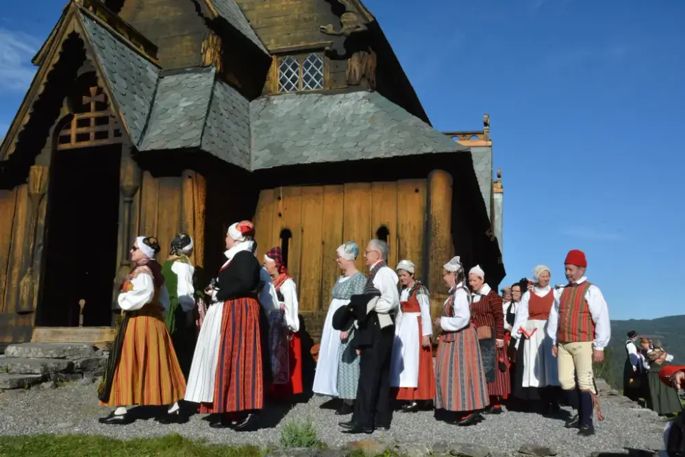 Gruppe mennesker i folkedrakter foran en stavkirke