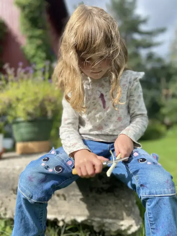 En jente i olabukse sitter å spikker 